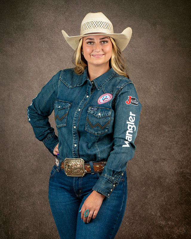 Emma Stowe smiling at the camera, posing wearing a denim shirt and cowgirl hat.